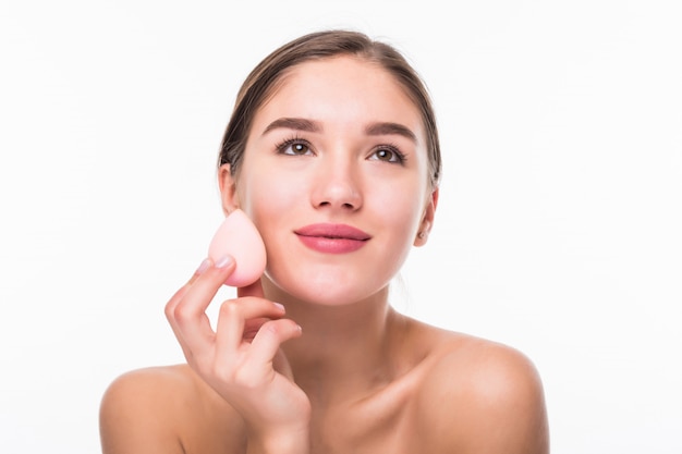 Young pretty woman applying blusher on her face with powder puff isolated on white wall