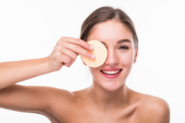 Young pretty woman applying blusher on her face with powder puff isolated on white wall