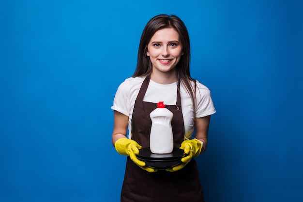 Foto gratuita giovane donna graziosa in grembiule con piatti lavati e detersivo per piatti. una bottiglia di detersivo per i piatti con un'etichetta vuota su una pila di piatti puliti