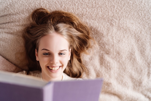自宅のベッドでお気に入りの本を楽しんでいる若いきれいな女性
