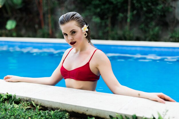 Young pretty woman in bikini relaxing at swimming pool edge poolside.