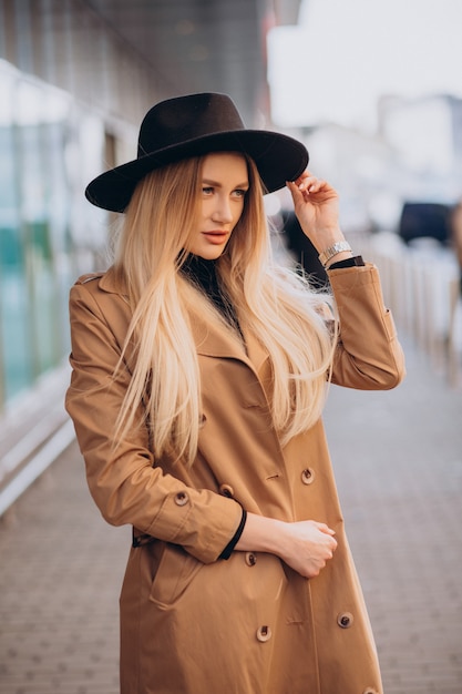 Молодая красивая женщина в черной шляпе и бежевом пальто гуляет по торговому центру