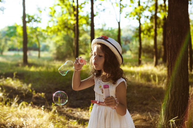 Young pretty woman blowing bubbles, walking in park at sunset