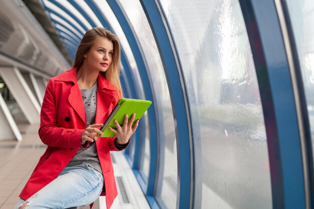 Young pretty woman in casual outfit holding tablet laptop in urban building
