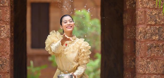 Free photo young pretty woman dress in beautiful thai costumes splashing water in temples and preserve the good culture of thai people during songkran festival thai new year family day in april