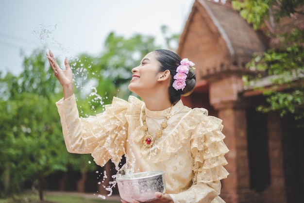若いきれいな女性は、寺院で水をはねかける美しいタイの衣装を着て、4月のソンクラン祭りタイ新年家族の日にタイの人々の良い文化を保存します