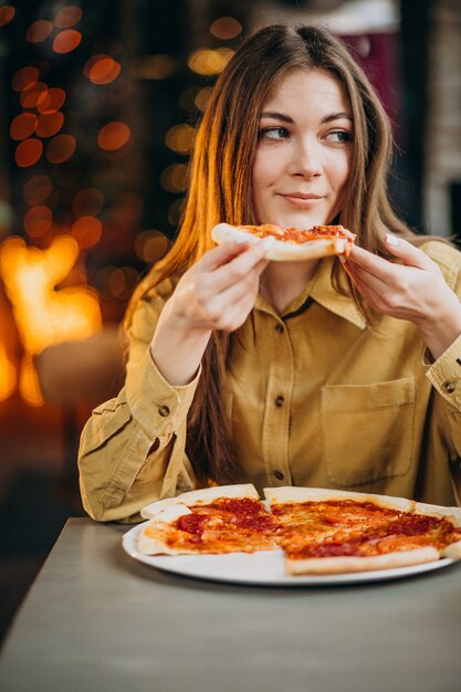 Молодая красивая женщина ест пиццу в баре