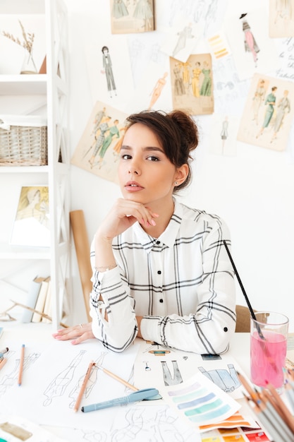 Foto gratuita giovane stilista grazioso della donna che si siede al suo scrittorio del lavoro