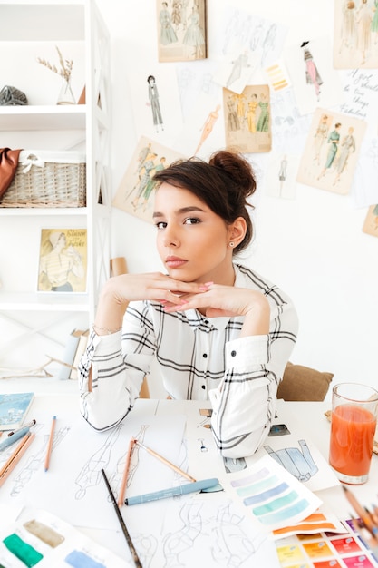 Foto gratuita giovane stilista grazioso della donna che si siede al suo scrittorio del lavoro