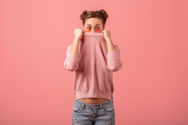 Young pretty woman fooling aroung with funny face expression in pink sweater and sunglasses isolated on pink studio background