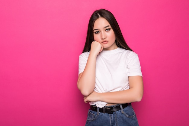 Young pretty woman frowning face in displeasure, keeps arms folded on pink wall