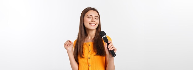 Бесплатное фото Молодая красивая женщина счастлива и мотивирована, поет песню с микрофоном, представляя событие или хавин