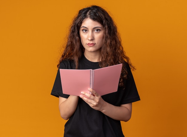 Free photo young pretty woman holding note pad looking at front isolated on orange wall with copy space