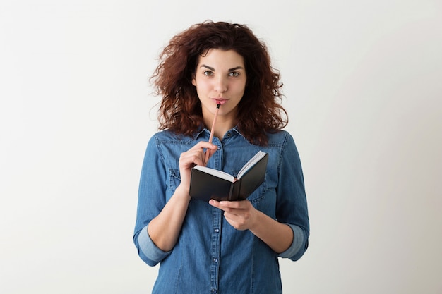 Free photo young pretty woman holding notebook, pencil at lips, thinking, smiling, curly hair, pensive, happy, isolated