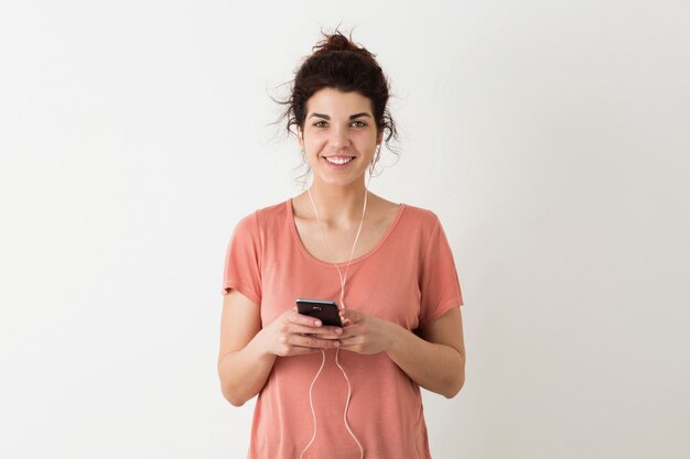 Young pretty woman holding smartphone, listening to music on earphones, smiling, positive, happy, isolated, pink t-shirt