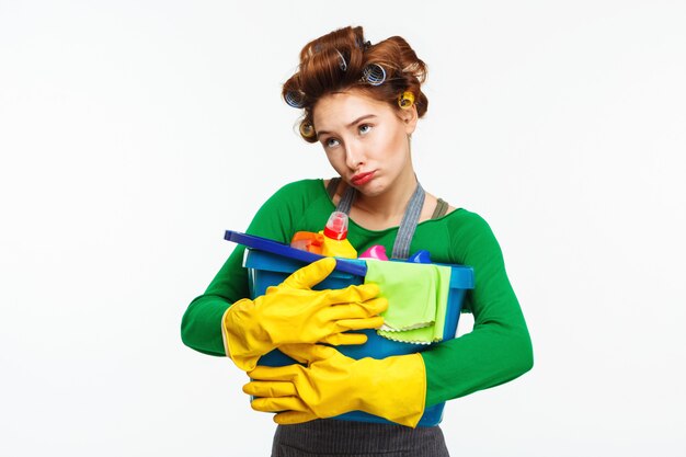 Young pretty woman holds cleaning tools with sadness on face