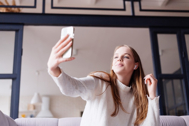 Giovane bella donna a casa sul divano che scatta foto selfie