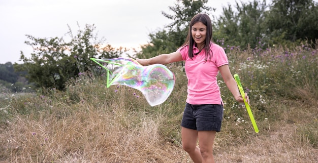 A young pretty woman launches large colored soap bubbles among the grass in nature.