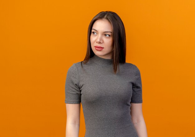 Young pretty woman looking at side isolated on orange background with copy space