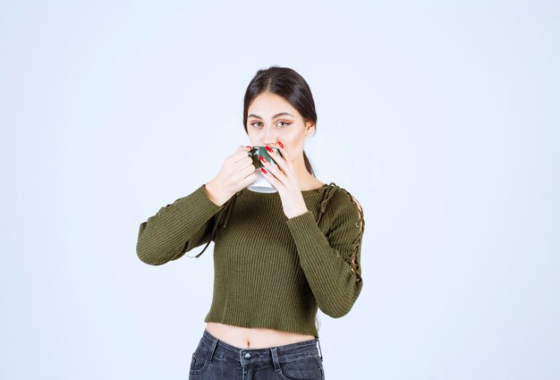 Un modello di giovane donna graziosa che beve da una tazza e guarda la telecamera.