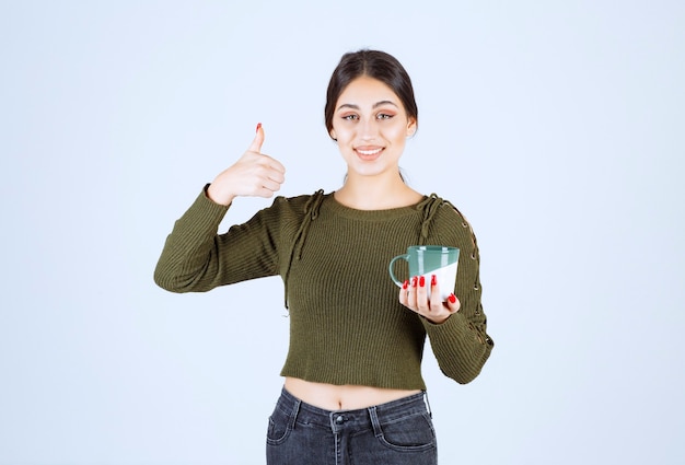 A young pretty woman model holding a cup of hot drink and showing a thumb up.