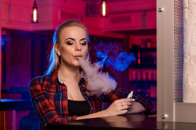 Молодая красивая женщина в рубашке в клетке курит электронную сигарету в вейп-баре. Вейп магазин.