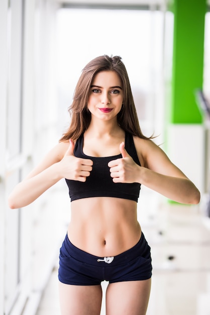 Young pretty woman shows thumbs up sign in sport centre gym