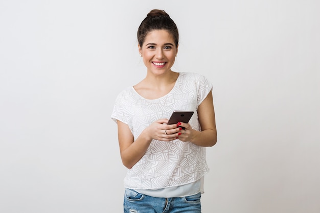 Молодая красивая женщина улыбается в белой футболке, держа и используя смартфон, мобильное устройство, изолированные