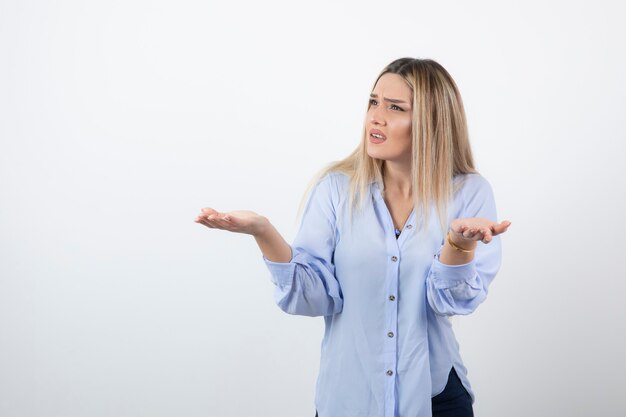 Young pretty woman standing and arguing with someone on white wall.