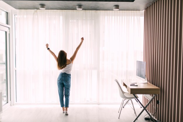 Young pretty woman stretching at home in front of window in the morning