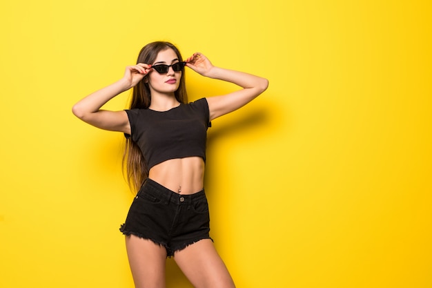 Young pretty woman in sunglasses posing on yellow wall