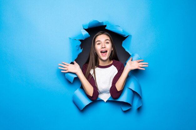 Young pretty woman surprised looking through blue hole in paper wall.