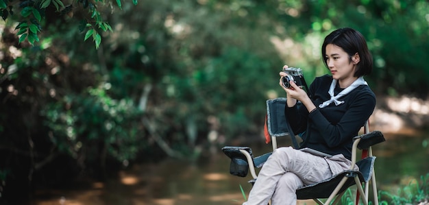 若いきれいな女性は、幸福のコピースペースで森でキャンプしながら美しい自然の写真を撮るデジタルカメラを使用しています
