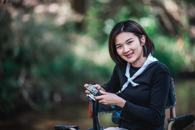 La giovane donna graziosa usa la fotocamera digitale per scattare una foto bella natura mentre si accampa nella foresta con lo spazio della copia di felicità