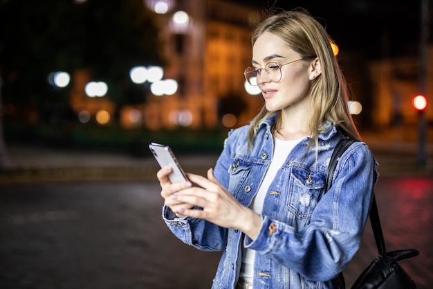Giovane donna graziosa che utilizza smartphone nella città alla notte