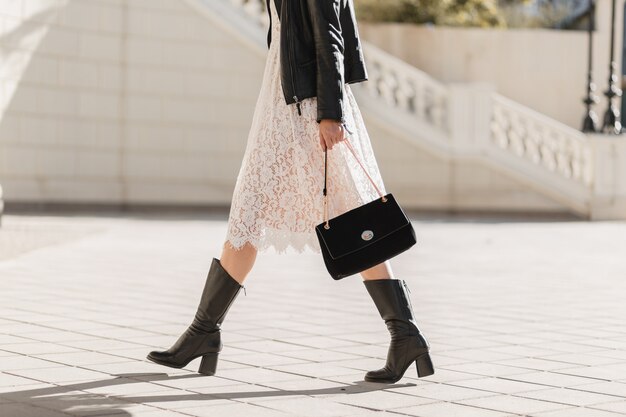 Young pretty woman walking in street in fashionable outfit, holding purse, wearing black leather jacket and white lace dress, spring autumn style, warm sunny weather, romantic look