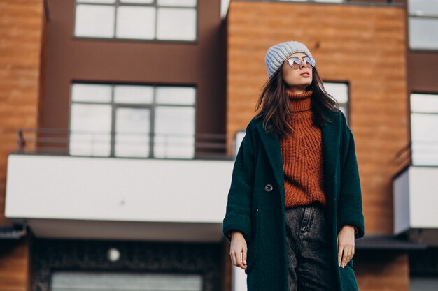 Young pretty woman in warm coat by the house