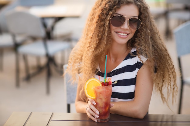 Giovane donna graziosa con un cocktail nella terrazza del caffè