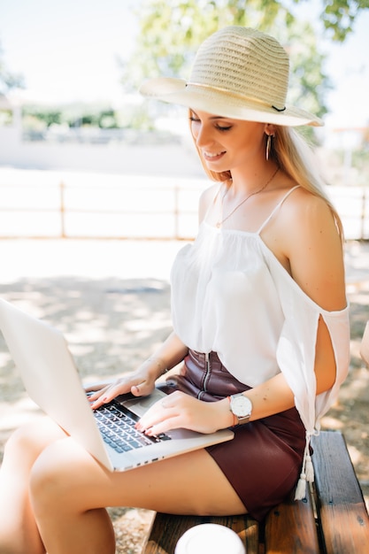 Молодая красивая женщина с ноутбуком на скамейке в парке