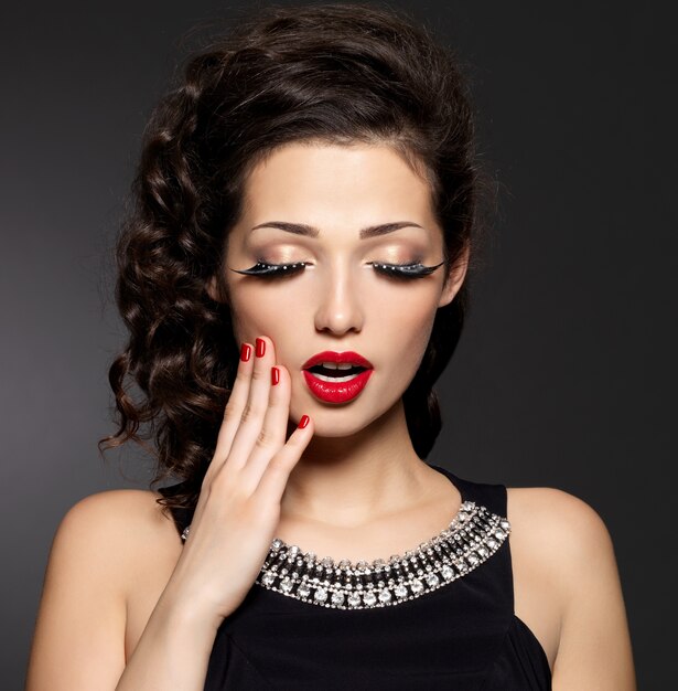 Young pretty woman with red manicure,  lips and creative eye makeup.  Fashion model with bright expressions