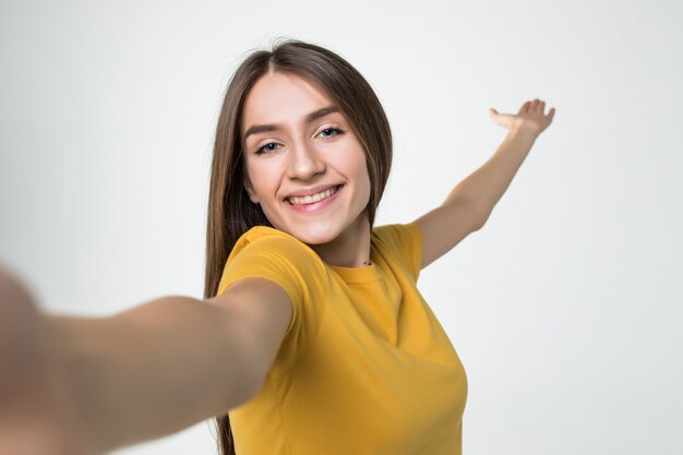 흰 벽에 고립 된 휴대 전화에 selfie을 복용하는 젊은 예쁜 여자