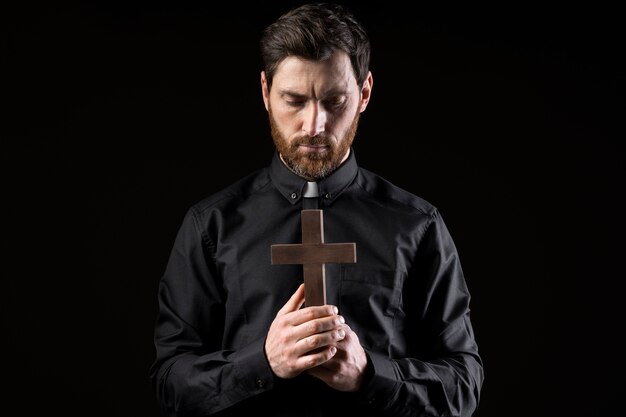 Young priest praying with cross medium shot