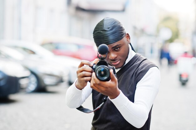 プロの機器を備えたプロのカメラを持っている若いプロのアフリカ系アメリカ人のビデオグラファー黒のduraqを身に着けているアフロカメラマンがビデオを作っています