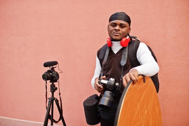 プロの機器を備えたプロのカメラを持っている若いプロのアフリカ系アメリカ人のビデオグラファー黒のduraqを身に着けているアフロカメラマンがビデオを作っています