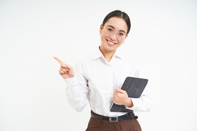 Young professional businesswoman in glasses holding digital tablet pointing finger left showing busi