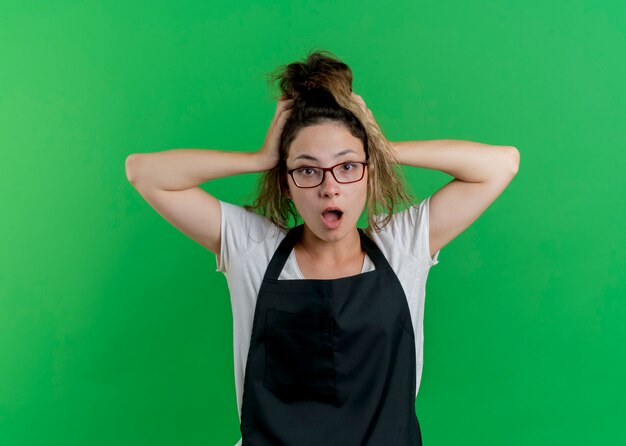 Foto gratuita giovane donna parrucchiere professionista in grembiule essendo frustrata tirandole i capelli