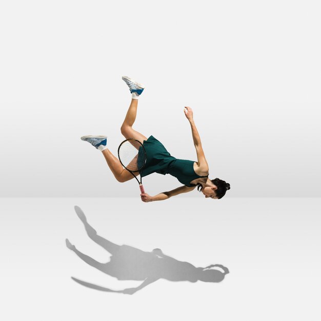 Young professional sportswoman levitating flying while playing tennis isolated on white wall