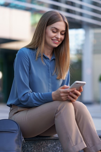 Young professional woman sitting on stair in front of glass building, talking on mobile phone