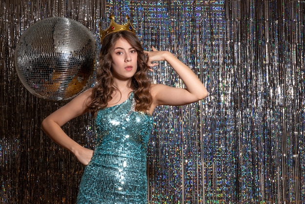 Young proud beautiful lady wearing blue green shiny dress with sequins with crown in the party