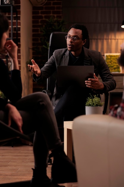 Free photo young psychotherapist explaining psychological issues to people at couple therapy, using laptop to take psychoanalysis notes. listening to conflict and finding solution to save marriage.